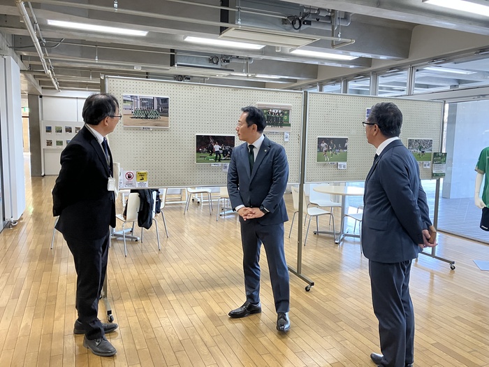 展示されている写真パネルを眺める東京ヴェルディの中村社長と栗田副社長