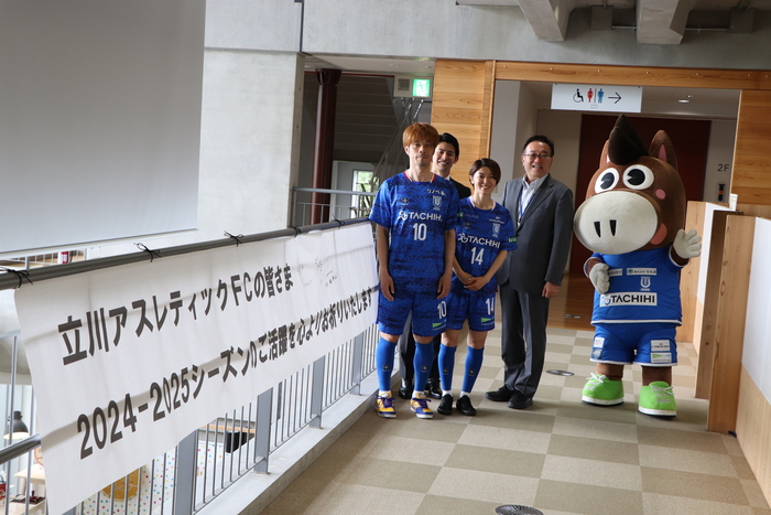 横断幕の横で集合写真撮影している立川アスレティックFCの皆さんと酒井市長