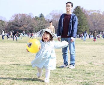 写真：ボールを持って走る女の子と見守る父親
