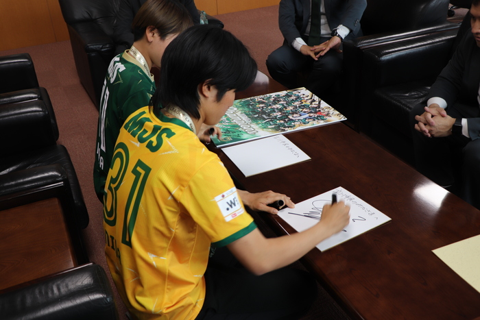 選手がポスターとカードにサインをする様子